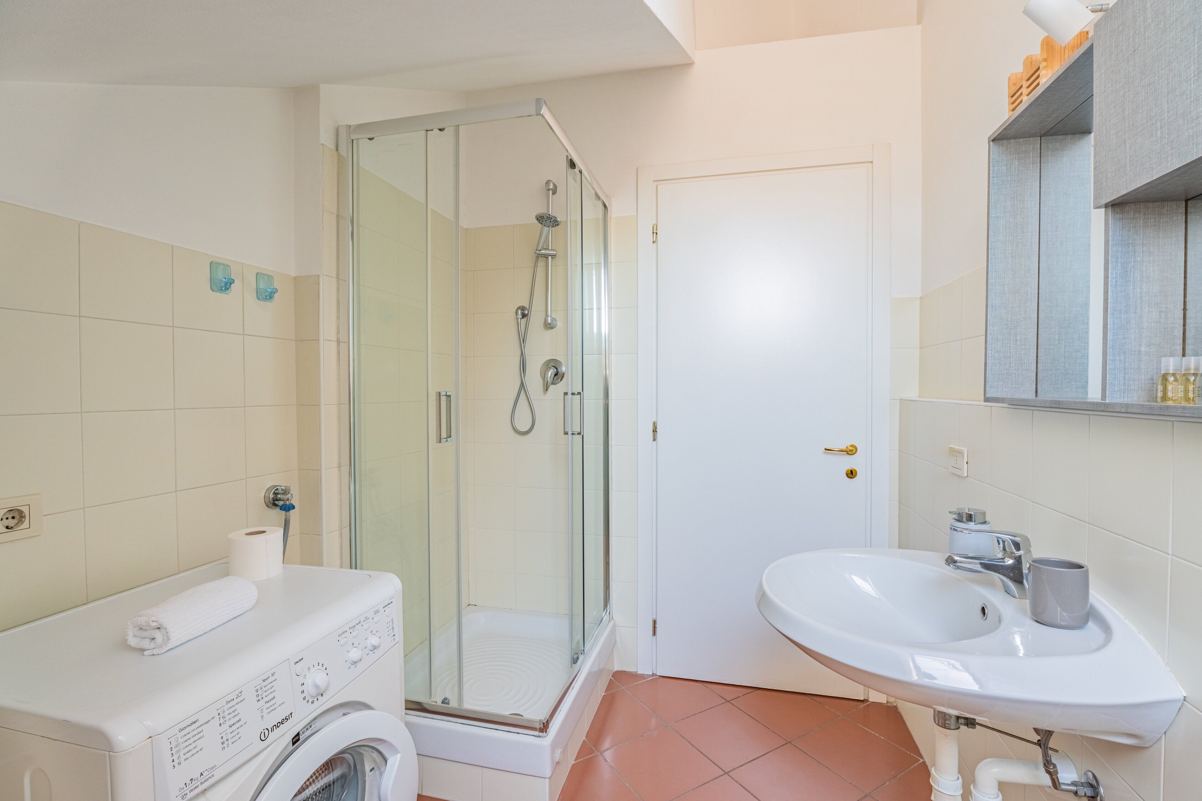 A bathroom with a glass-enclosed shower, a white sink, and a washing machine.