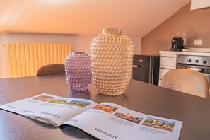 Ein Esstisch mit zwei strukturierten Vasen, einem Magazin, das auf der Seite 'Monforte' liegt, und einer Küche im Hintergrund.