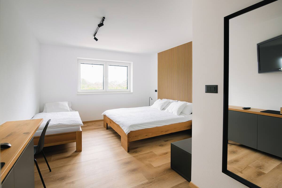A modern bedroom with two beds, a desk, and a TV.