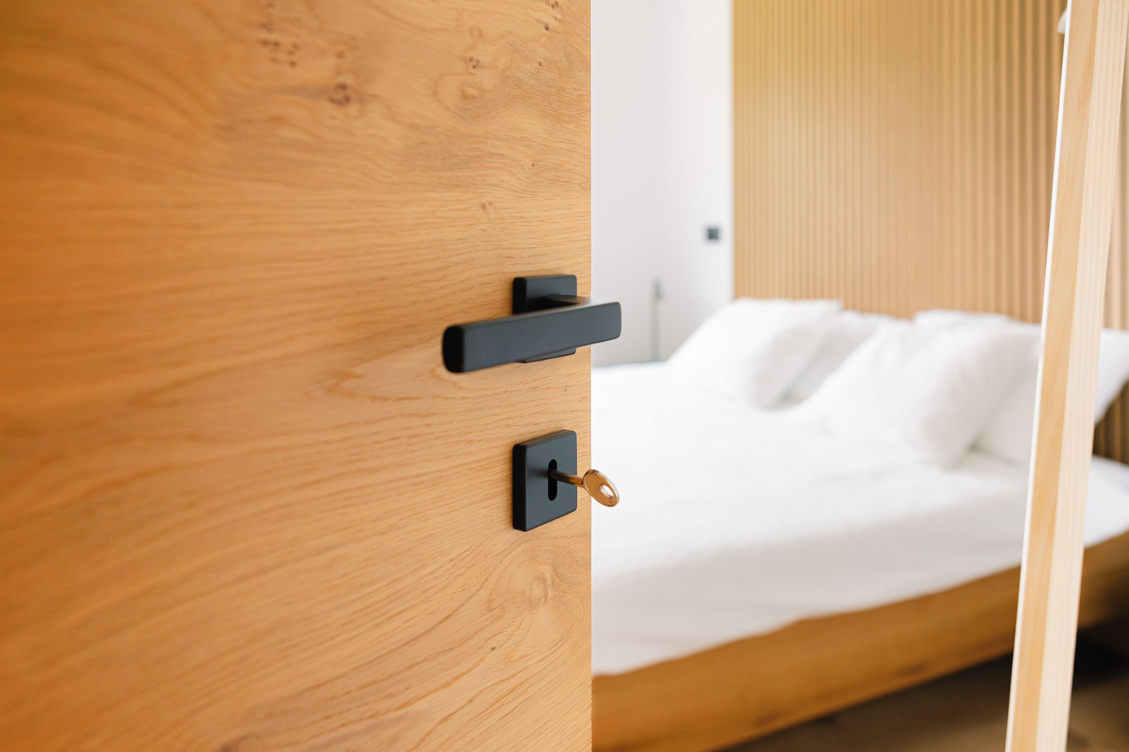 Una puerta de madera con manija y cerradura negros, que da a una cama con ropa blanca.
