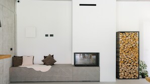 A modern living room with a built-in bench, a fireplace, and a stack of firewood.
