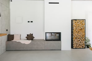 A modern living room with a built-in bench, a fireplace, and a stack of firewood.
