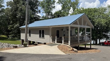 A small, single-story building with a blue roof, a porch with chairs, and a sign reading 'BAY SIDE YACHT SALES.'