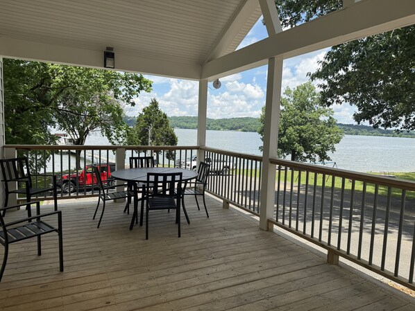 A covered outdoor area with a table and chairs, a railing, and a view of a lake.