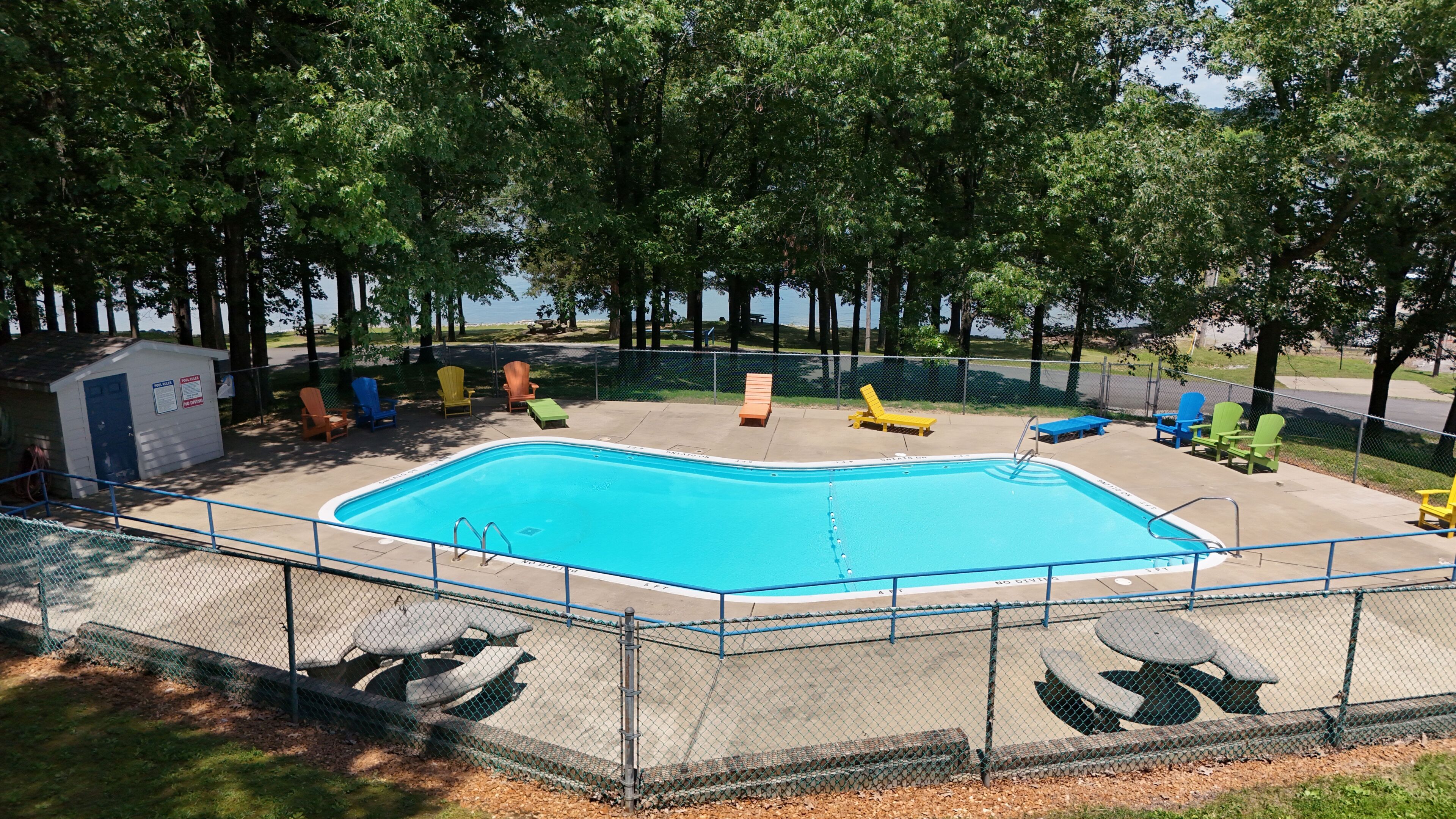 A swimming pool with a fenced deck, lounge chairs, and a small utility shed.