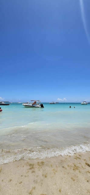 A beach with clear turquoise water, boats, and a sandy shore.