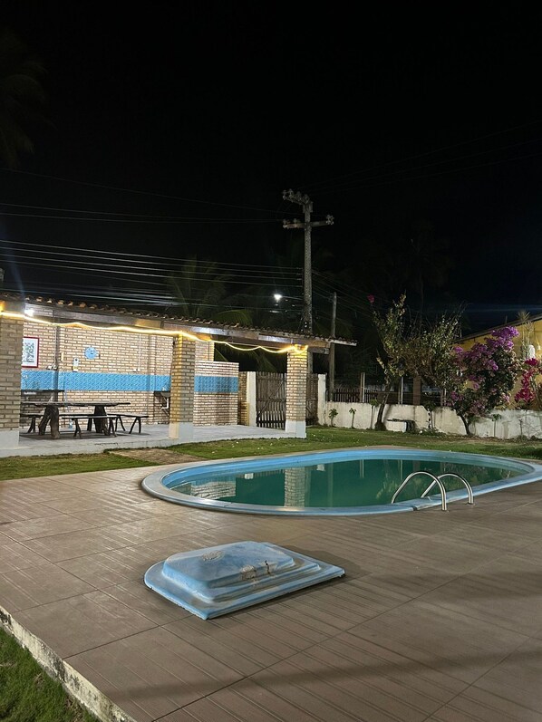 A swimming pool area with a covered patio, a brick wall, and a fence.
