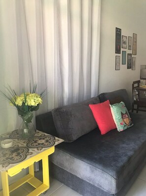 A living room with a sofa, a small table with a vase of flowers, and a wall with framed pictures.