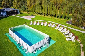 Una piscina rectangular con un deck perimetral, rodeada por un césped cuidado y una fila de sillas reclinables blancas.