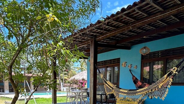 Un espace extérieur abrité, doté d’un coin salon, d’un hamac, d’une piscine et d’un bâtiment à la façade bleue.