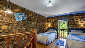 Una habitación con paredes de piedra, suelo de madera, dos camas con cabeceros a juego, una escalera de madera y vistas a través de una puerta.