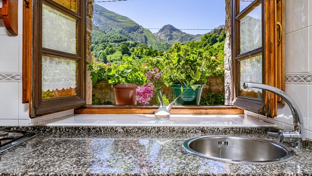 Una cocina con encimeras de granito, un fregadero de acero inoxidable y una ventana con vistas a montañas y vegetación.