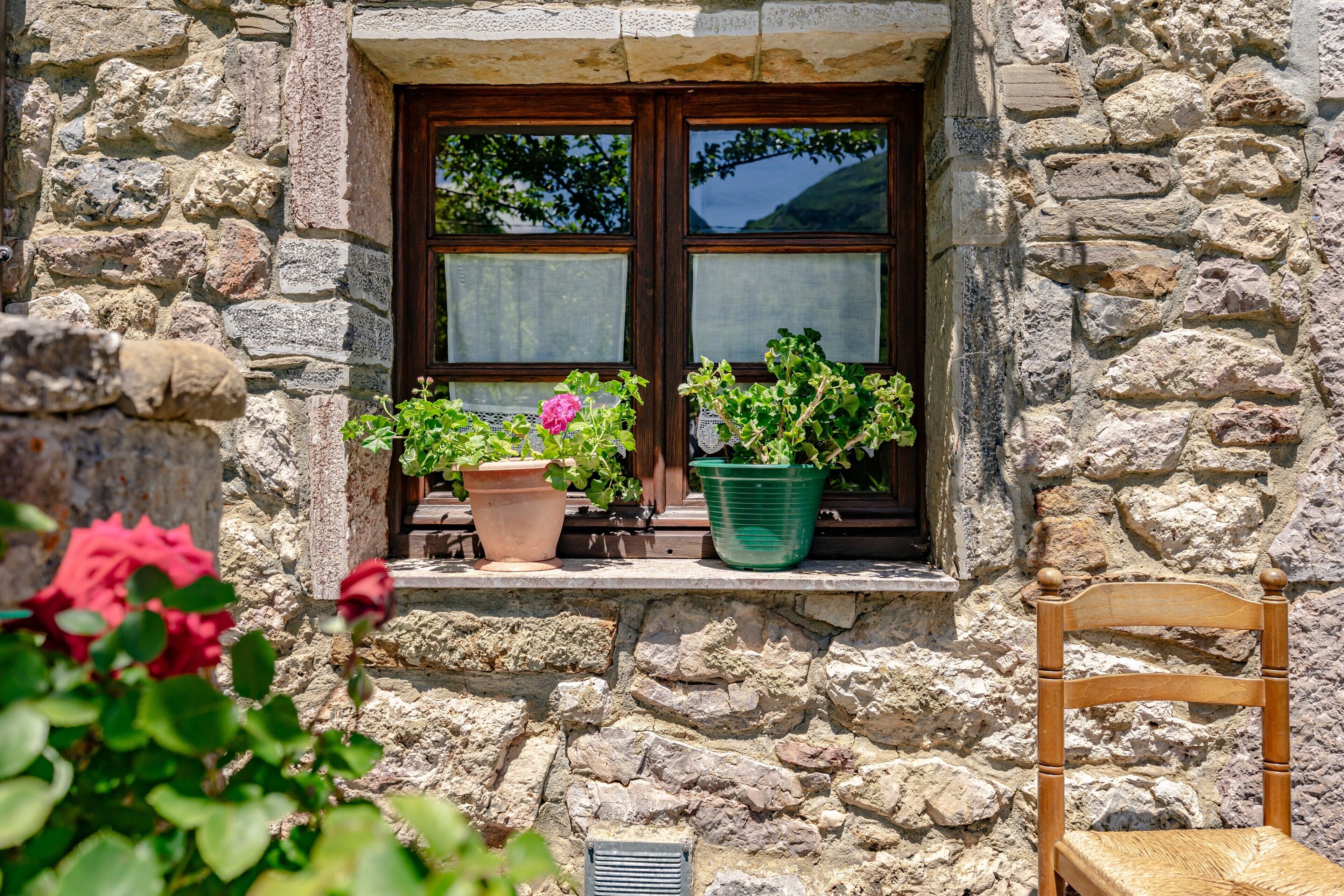 Un edificio de piedra con una ventana, plantas en macetas y una silla de madera.