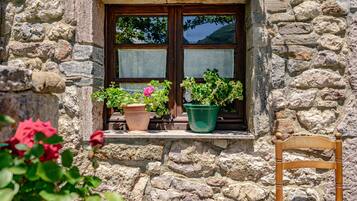 Un edificio de piedra con una ventana, plantas en macetas y una silla de madera.