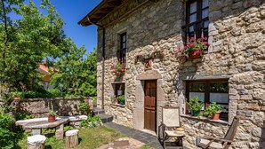 Un edificio in pietra con una porta di legno, finestre con persiane e un'area esterna con tavolo e sedie.