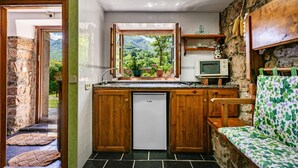 Una cucina compatta con frigorifero integrato, mobili in legno, un piccolo oblò con vista su piante e una parete in pietra.