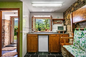 A compact kitchen with a built-in fridge, wooden cabinets, a small window with a view of greenery, and a stone wall. - Rural house with mountain views, shared garden, and Wi-Fi (Valle de Lago)