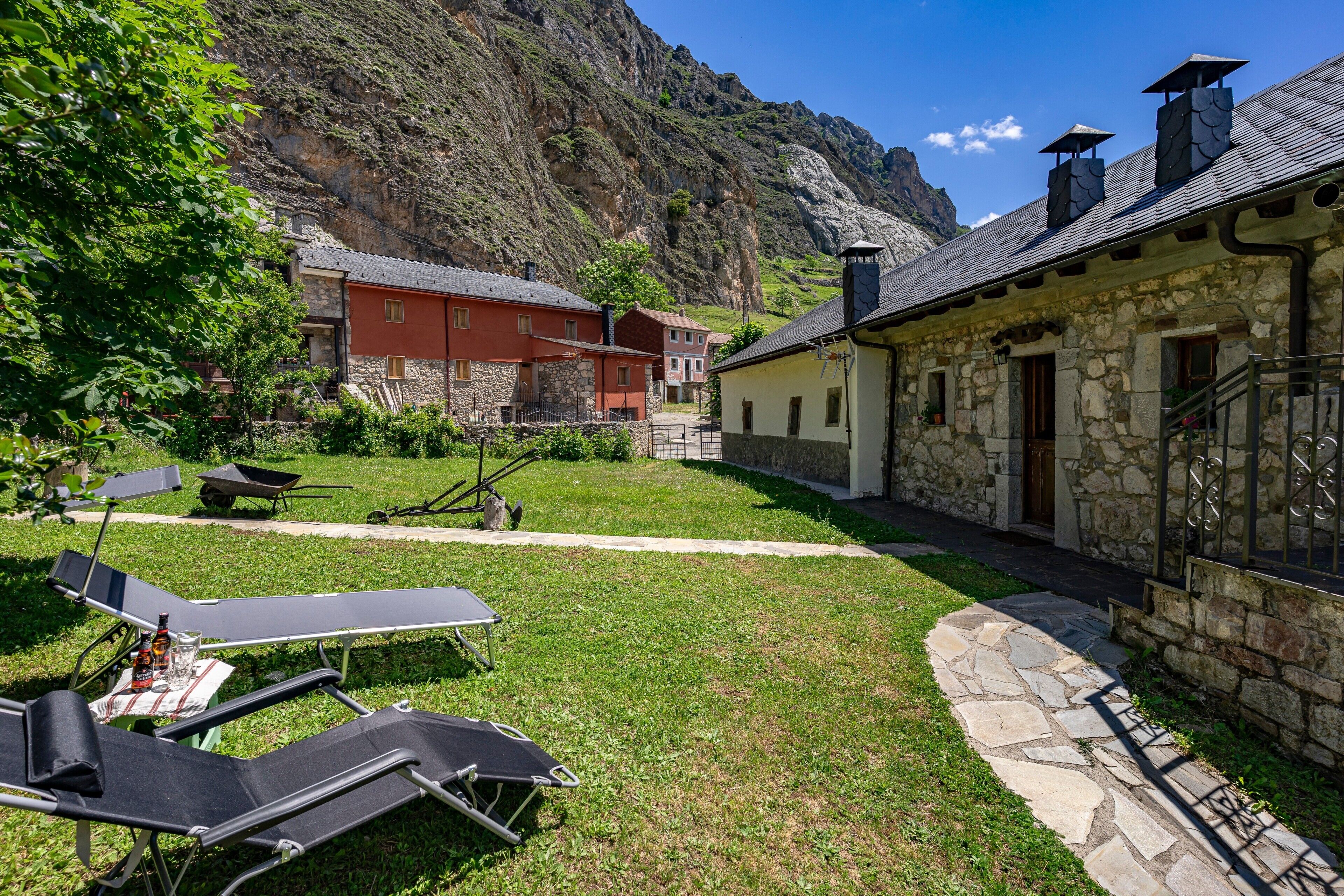 Un patio con mobiliario exterior, edificios de piedra y monta ñas al fondo.