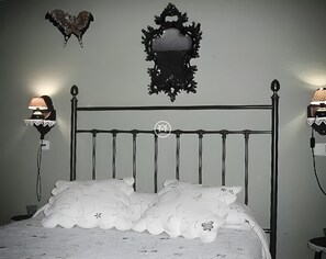 Un lit avec une tĂȘte de lit en mĂ©tal, deux lampes fixĂ©es au mur et un miroir dĂ©coratif placĂ© au-dessus du lit.