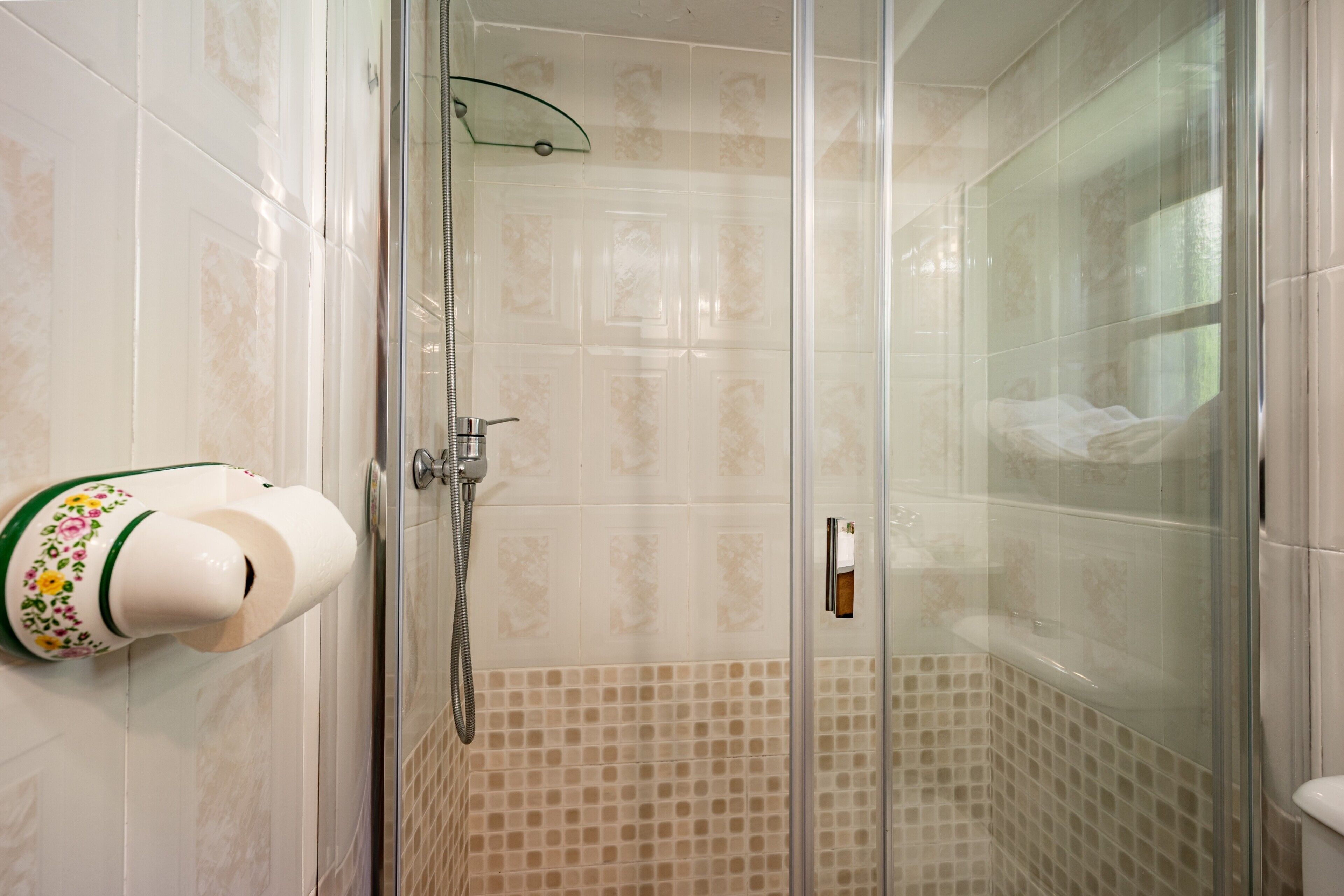 A shower with a glass door, a towel dispenser, and patterned tiles.