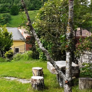 Paisaje rural con una casa, un árbol y un banco de piedra.