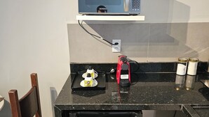 Eine kompakte Küchenzeile mit einer Mikrowelle, einem kleinen Kühlschrank, einer Kaffeemaschine und einem Toaster auf der Arbeitsfläche.