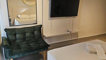 Une chambre d’hôtel équipée d’un lit, d’un canapé, d’un téléviseur fixé au mur et d’un climatiseur au plafond.