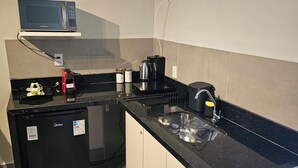 Eine kleine Küche mit Mikrowelle, Kaffeemaschine und Kühlschrank.