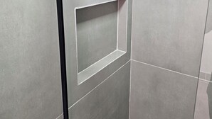 Eine Wand mit Fliesen, einer schwarzen Rohraußenleitung und einer eingelassenen Ablagefläche.