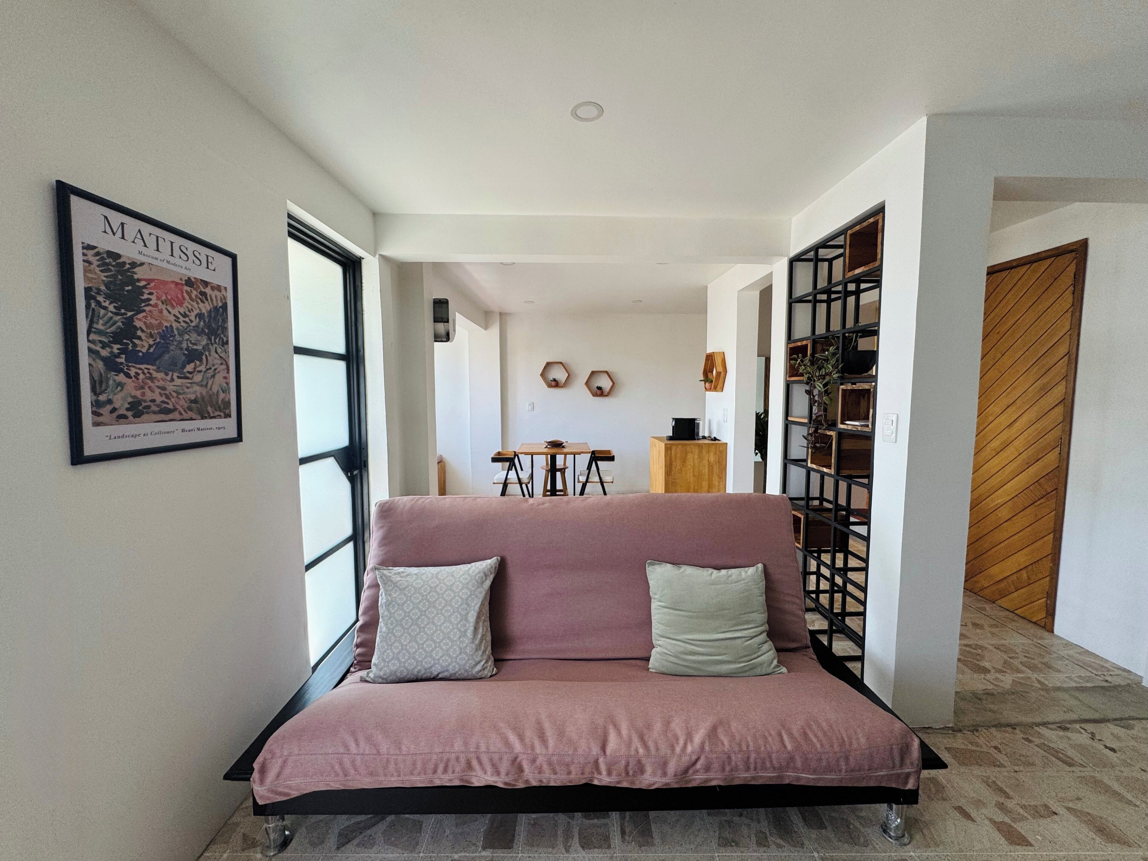 Ein modernes Wohnzimmer mit einem rosafarbenen Sofa, einem gerahmten Kunstwerk an der Wand und einem Essbereich im Hintergrund.