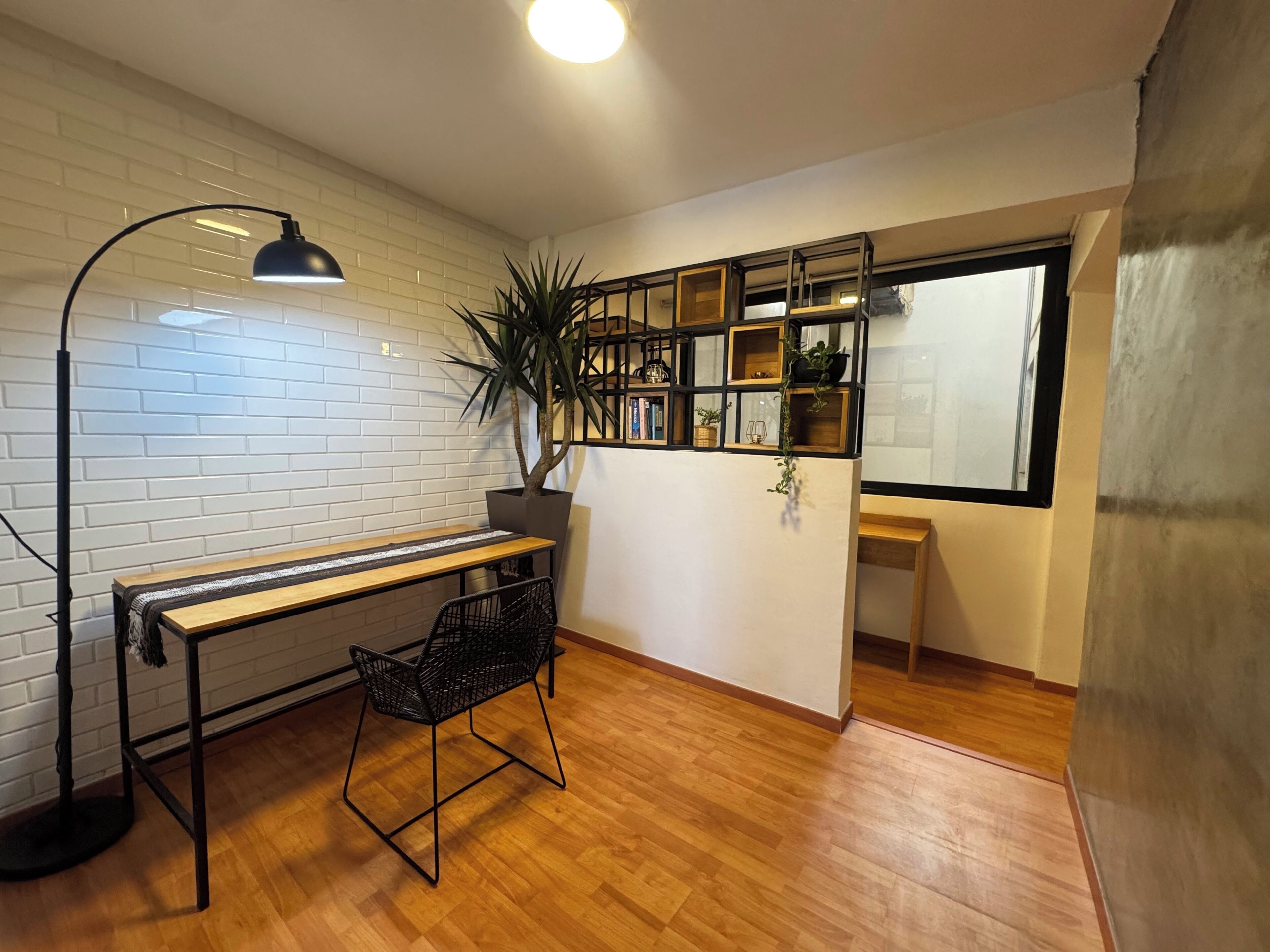Ein Zimmer mit Holzboden, Schreibtisch mit Stuhl, Blumentopf, Bücherregal und einem Fenster.