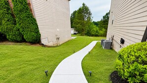 A pathway leading to a building with a brick chimney, surrounded by well-maintained grass and shrubs. - Cozy & Spacious 2BR Private Suite Near ATL Airport (Atlanta)