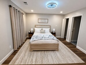 Ein Schlafzimmer mit Bett, Nachttischen, Deckenleuchte, Wanduhr und einer Tür.