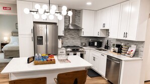 A modern kitchen with white cabinets, stainless steel appliances, a central island with bar stools, and a hanging light fixture. - Cozy & Spacious 2BR Private Suite Near ATL Airport (Atlanta)