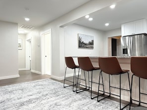 A modern kitchen with a stainless steel refrigerator, a bar area with four stools, and a hallway leading to another room. - Idyllic Cottage In Campobello by Tryon International (Campobello)