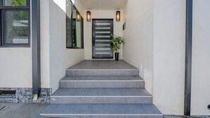 A modern entrance with a set of concrete steps leading to a door, a skylight above, and two wall-mounted lights.