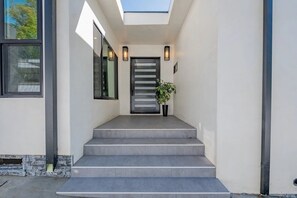 Una entrada moderna con una serie de escalones de concreto que conducen a una puerta, un tragaluz arriba y dos luces fijadas a la pared.