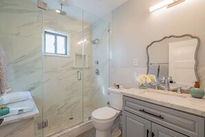 Ein Badezimmer mit einer Duschkabine, einer Toilette, einem Waschbecken mit Spiegel und einem Fenster.