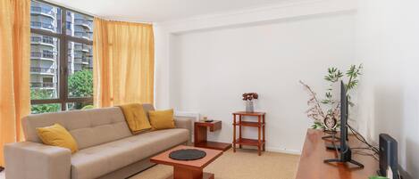 A modern living room with a sofa, coffee table, TV stand, and a window with curtains.