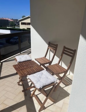 A balcony with wooden furniture, including a table and chairs, and a view of buildings in the background. - Apartment 'On Amorosa Beach' with Sea View, Shared Garden and Wi-Fi (Neiva)