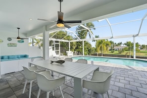 Ein Poolbereich mit überdachter Terrasse, weißen Korbmöbeln und Deckenventilator.