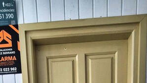 Eine beigefarbene Tür mit Schlüsselloch und Türknauf, eine braune Fußmatte und ein Schild mit Kontaktinformationen an der Wand.