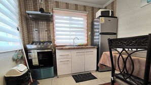 Une cuisine compacte équipée d’une cuisinière, d’un four, d’un four à micro-ondes et d’un réfrigérateur, ainsi que d’un coin repas avec une table et une chaise.