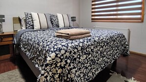 Une chambre à coucher avec un lit, une table de chevet, une lampe, un tableau encadré au mur et une fenêtre avec des stores.
