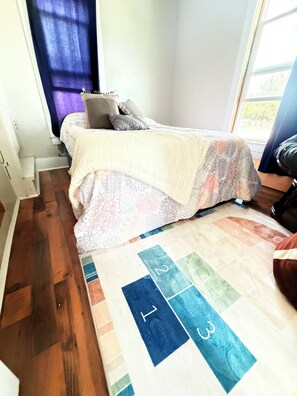 A bedroom with a bed, a window, a door, and a wooden floor.