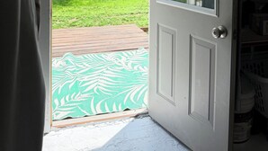 A white door with a window, a green patterned mat, and a view of a grassy yard with a building in the background. -     Rustic Spa Escape Near I-70 (Goodland)