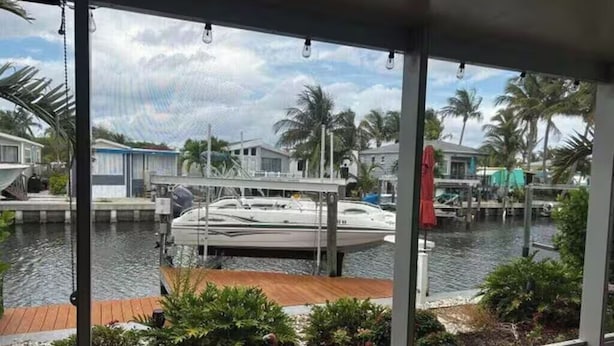 Een jachthaven met afgemeerde boten, een houten steiger en een uitzicht op de omgeving, inclusief huizen en palmbomen.