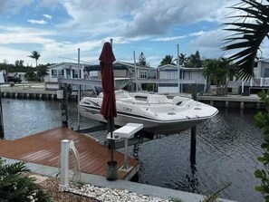 A boat docked at a marina with a wooden deck, a covered area, and a residential building in the background. - Aqua Tide Retreat - Waterfront + Boatlift (Jensen Beach)