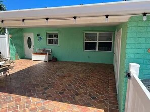 A covered patio area with a brick floor, a white door, and a window. - Aqua Tide Retreat - Waterfront + Boatlift (Jensen Beach)