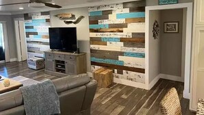 Een woonkamer met een flatscreen televisie, een bank, een salontafel, een houten vloer en een wand met een horizontaal houten lambrisering.